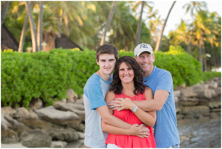family hugs under palm tree at Ko olina