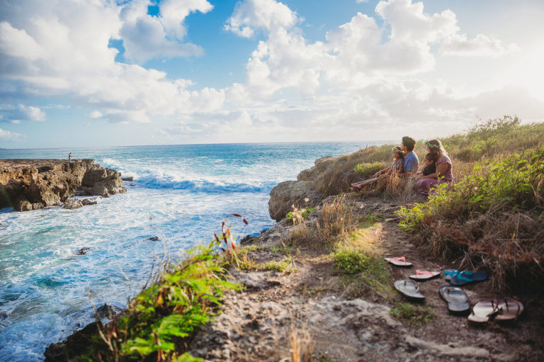 family sitting on edge of cliff watching the ocean waves