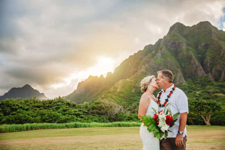 A kiss between a couple with hawaiian mountains behind them