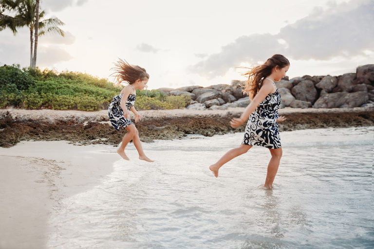 two girls wearing hawaiian print dresses running in to the lagoon at Ko Olina
