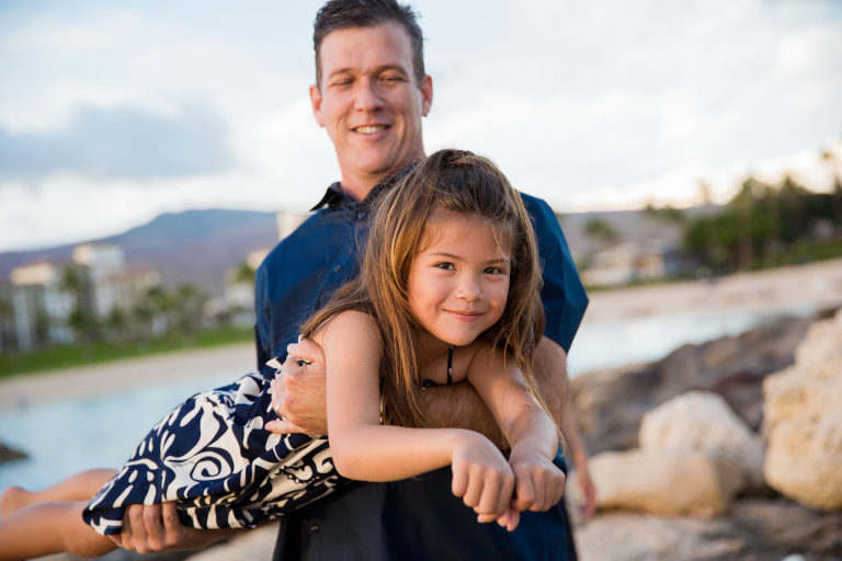 little girl in hawaiian print dance playing airplane with dad by Ko Olina lagoon